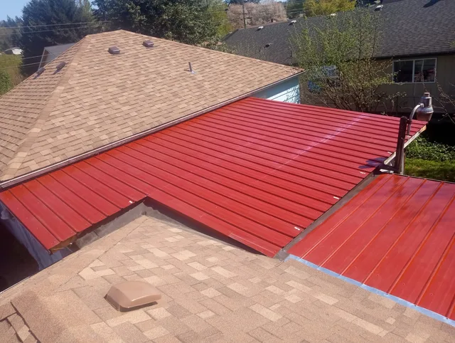 Red panel metal roof joined into an existing tan shingle roof